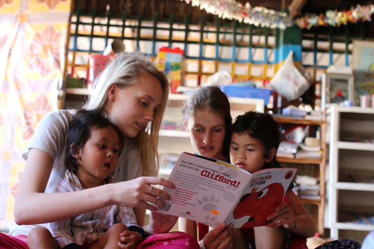 Female volunteers on the Projects Abroad Childcare Programme read a book to two local Cambodian children.