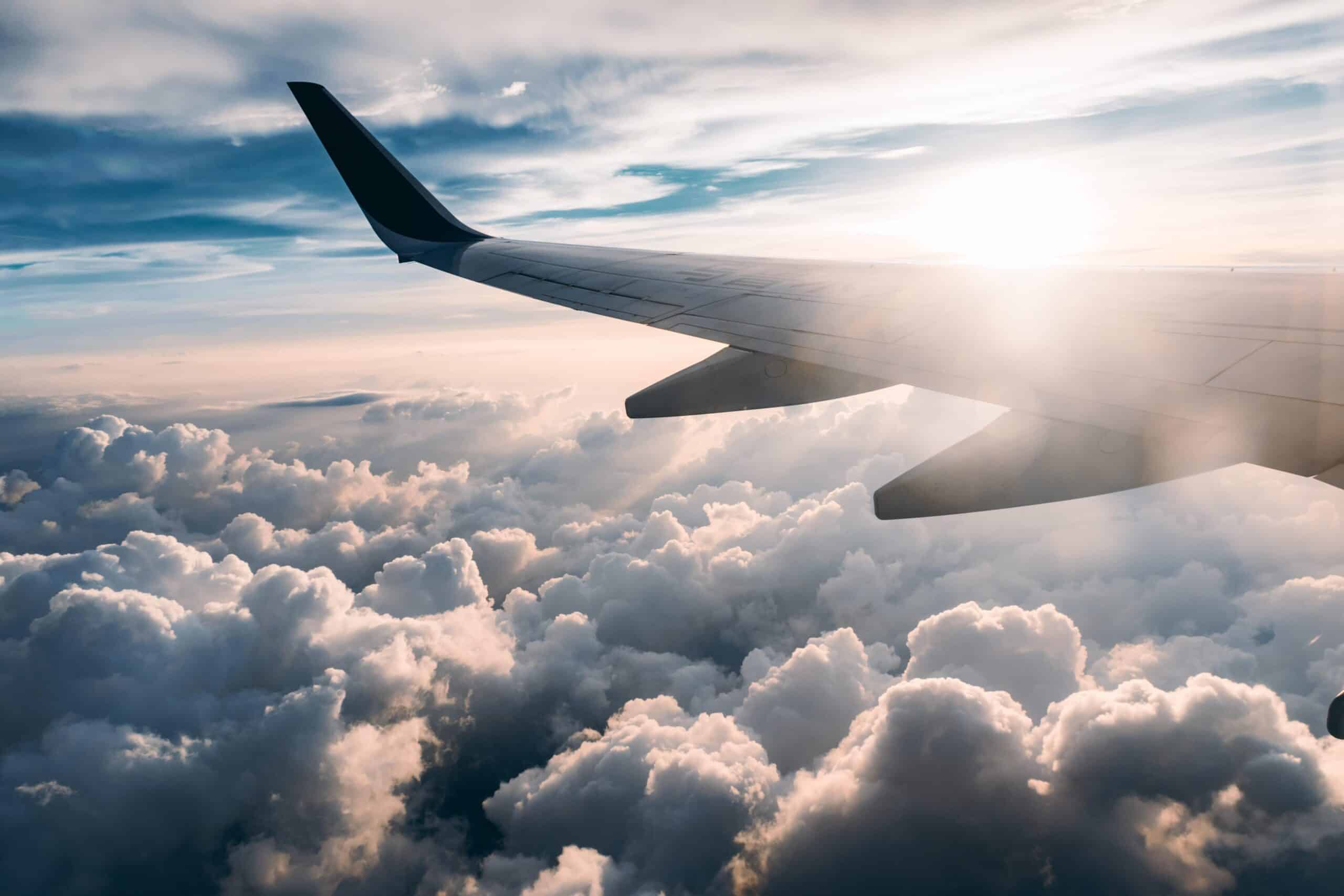 Airplane wing over cloud with sun shining.