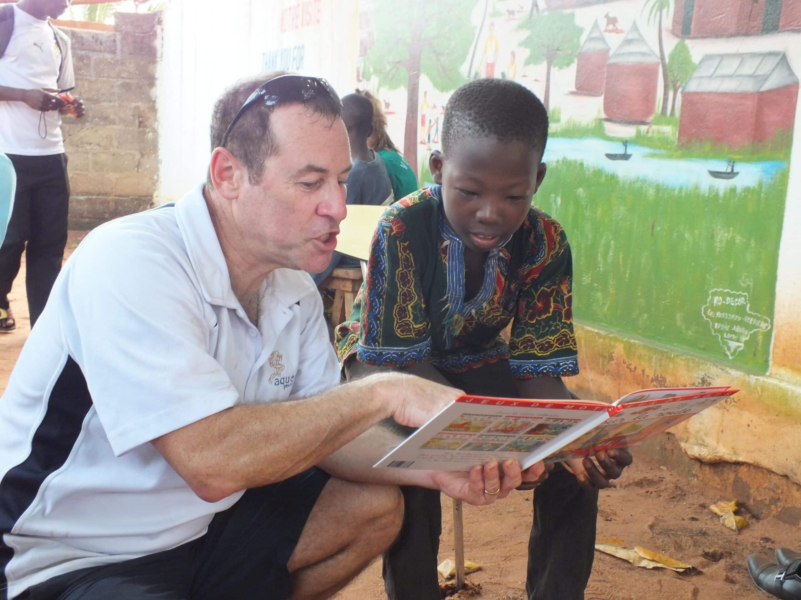 An older Projects Abroad volunteer reads to a child in Africa.