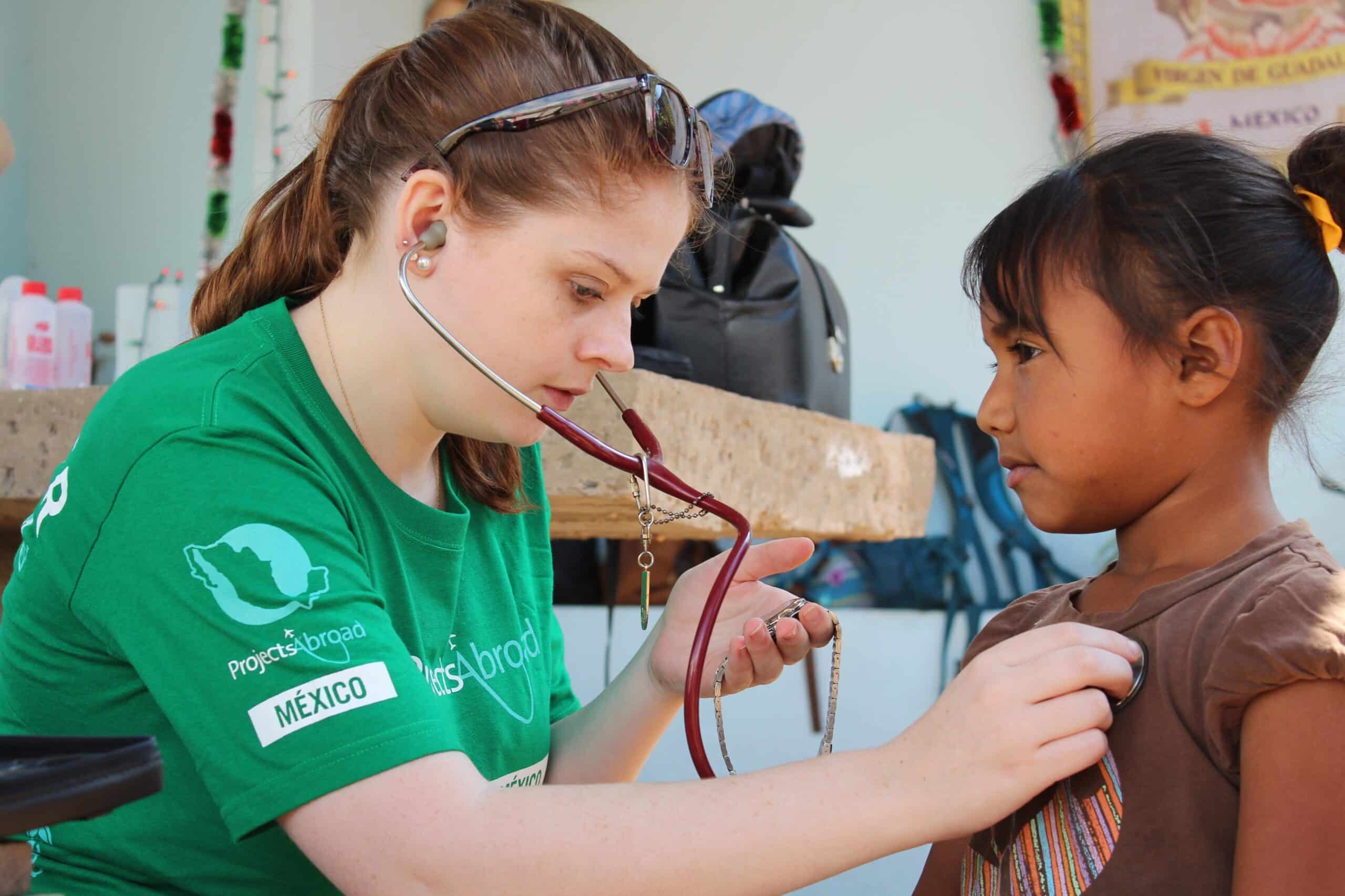A volunteer measures the heartbeat of a young girl during her medical internship abroad for high school students.