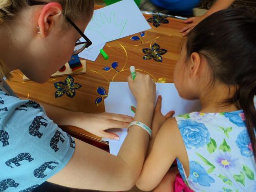 Projects Abroad volunteer working with children in Mongolia helps a child draw around their hands during an educational acitivity.