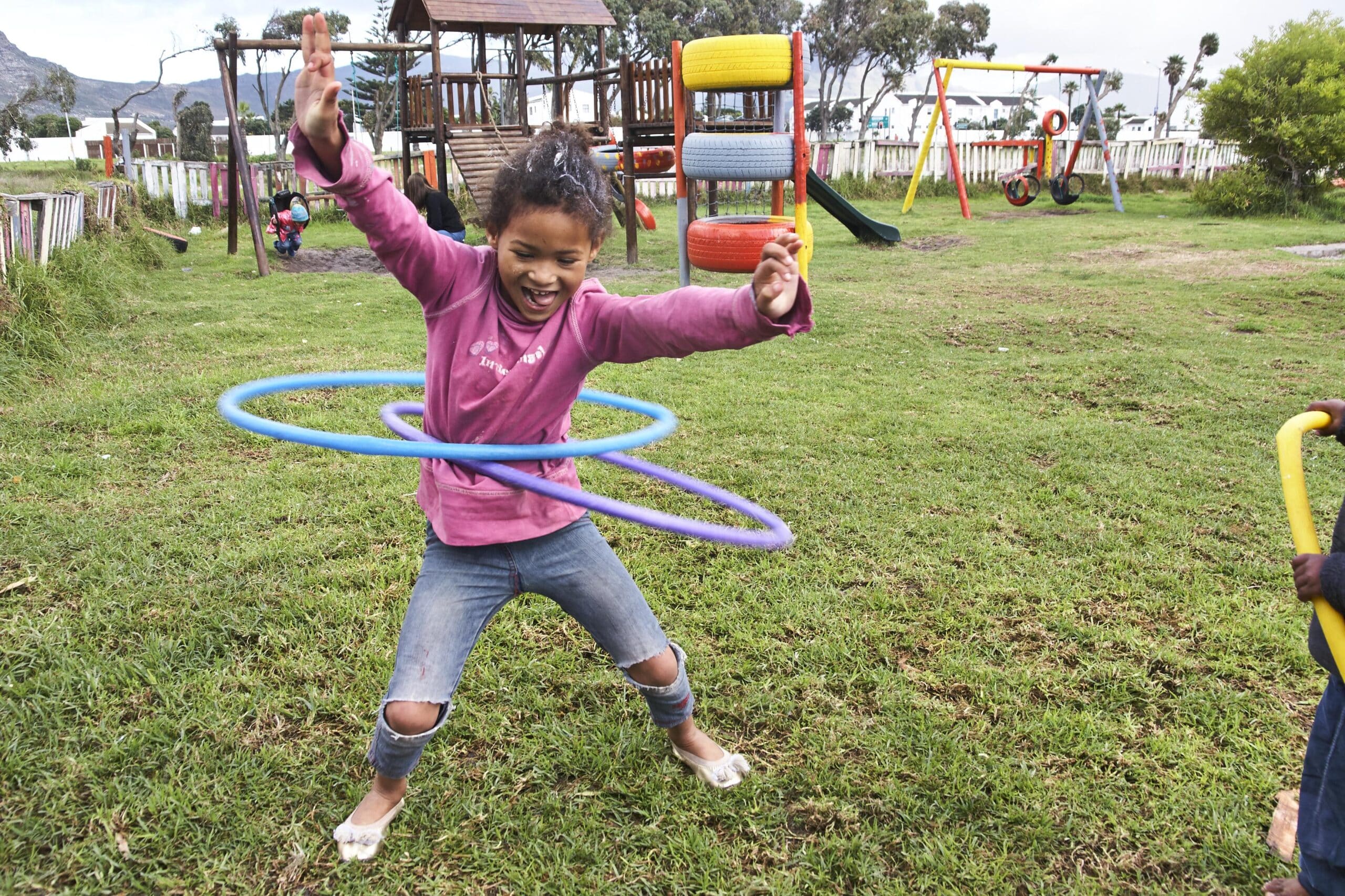 During a Childcare Project in South Africa, a young girl hula hoops outside a care centre.