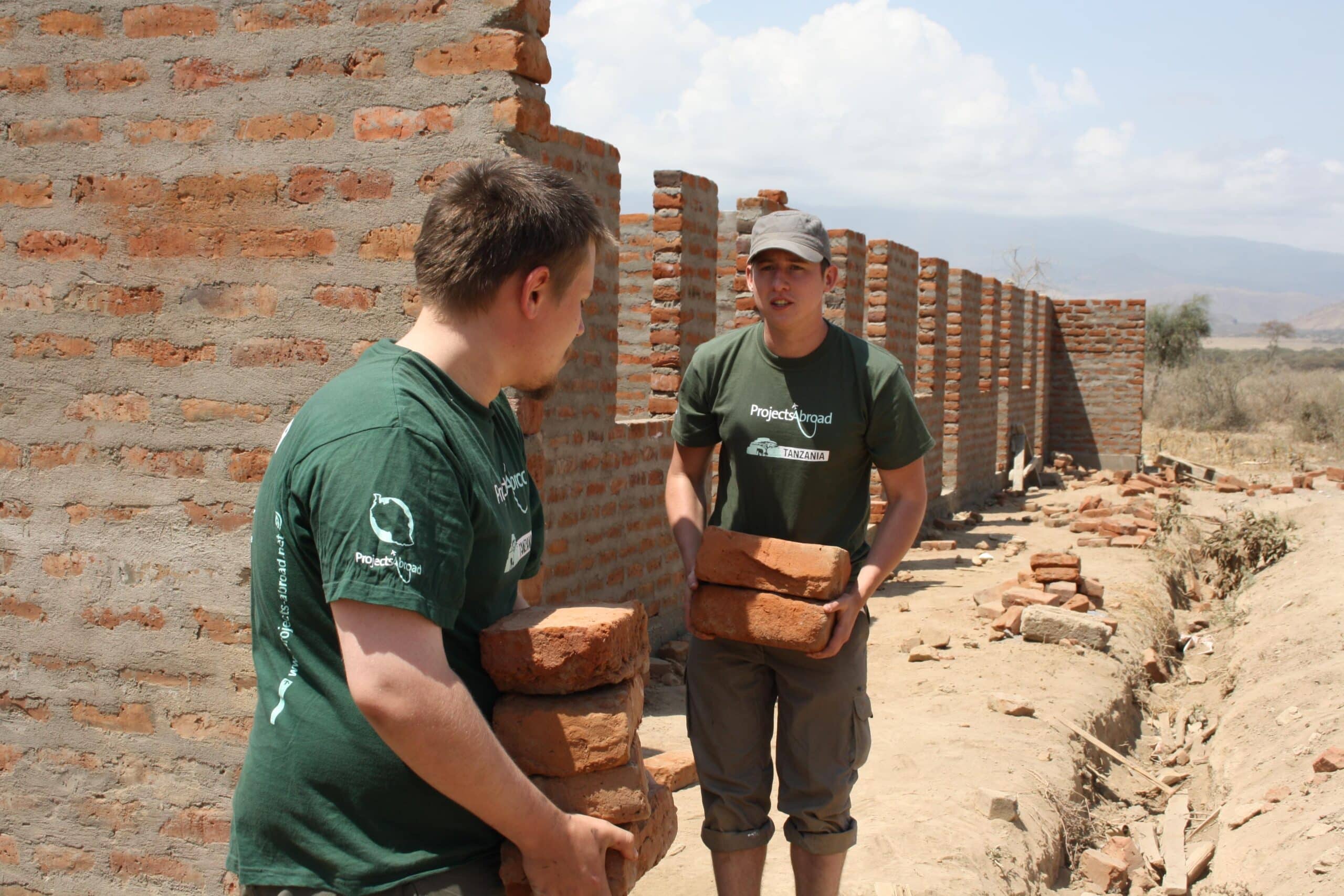Teenage volunteers doing construction work in Tanzania carry bricks needed for a wall.