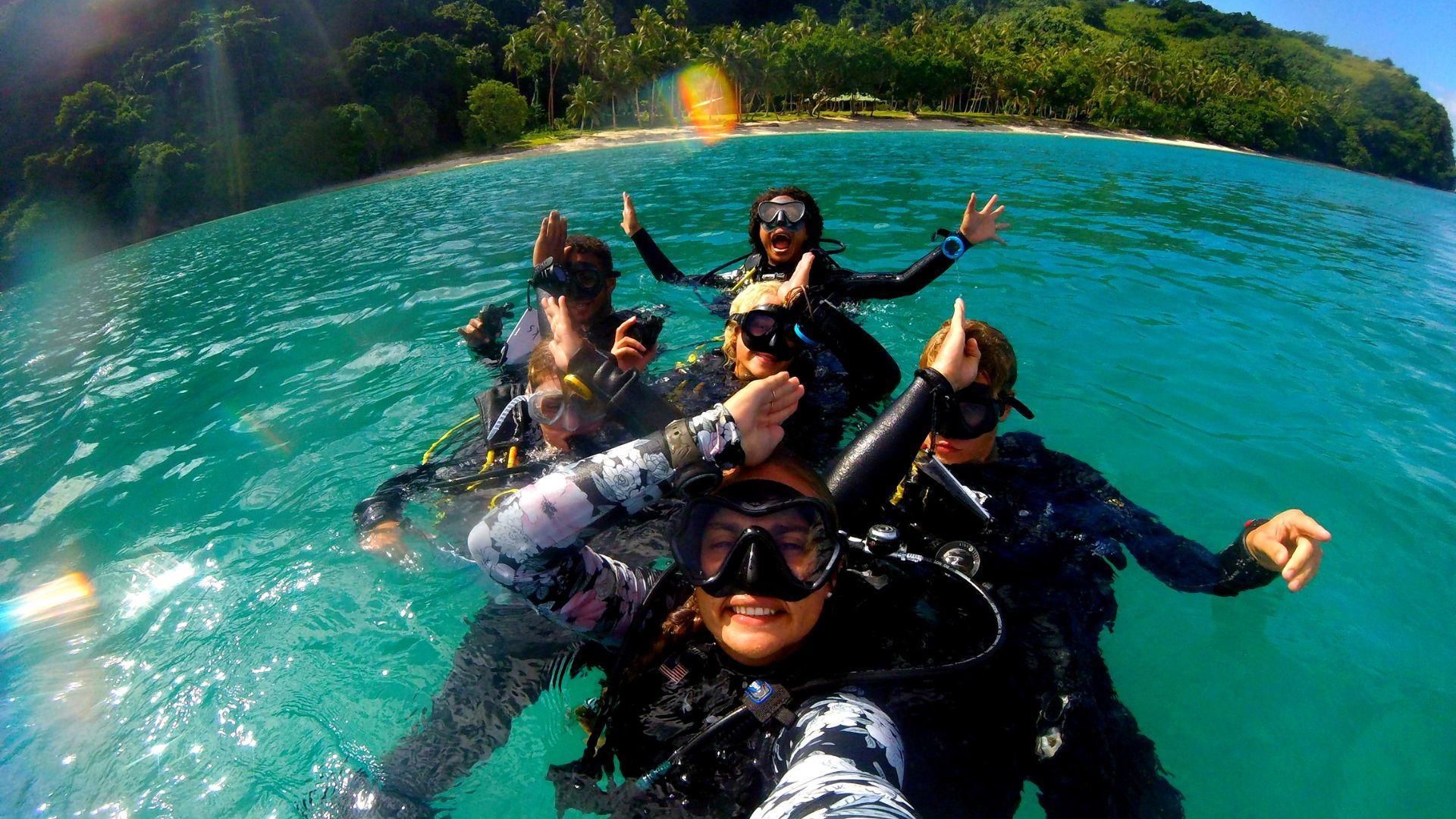 A Projects Abroad group of six in Fiji snorkel together, holding their hands up above their head like a shark's fin